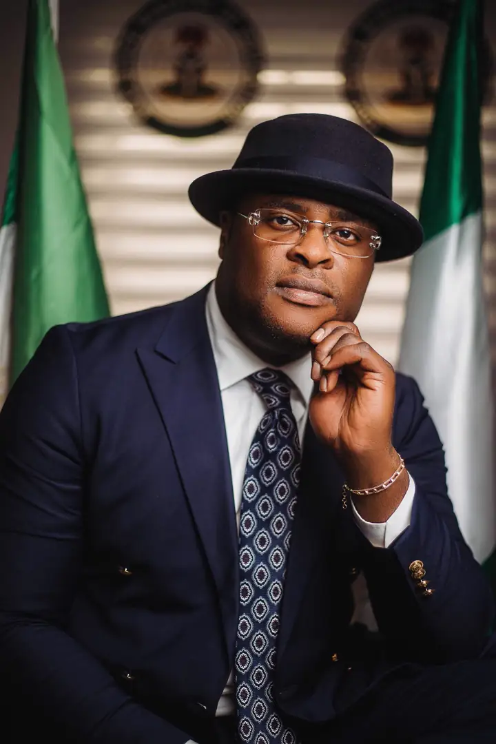 Dr Paddy Iyamu seated in a fedora in front of Nigerian flags